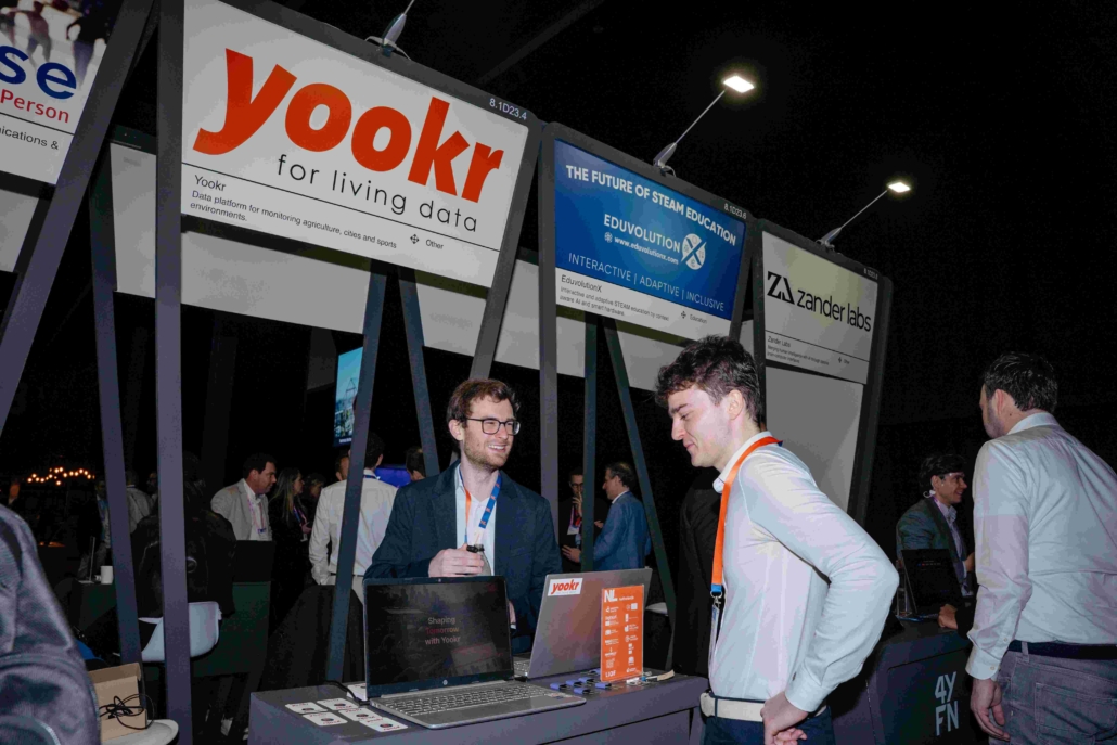 A picture of a person visiting a Yookr stand and talking to a smiling colleague.