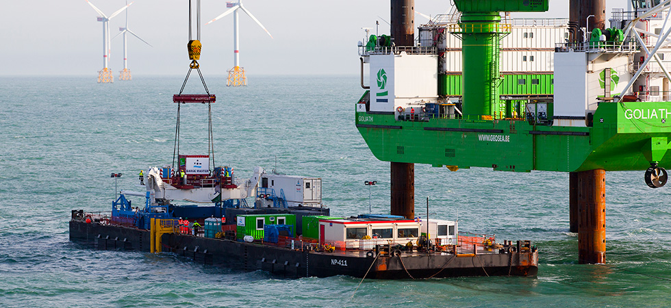 Een echte foto van een schip van Barge Master dat onderdelen naar een boorplatform op zee brengt. Naast een windmolenpark.