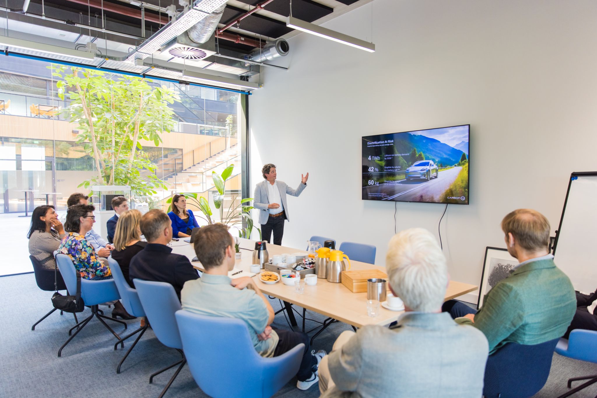 Een foto van een CarbonX werkbezoek, het team zit rond een tafel naar een scherm te kijken.