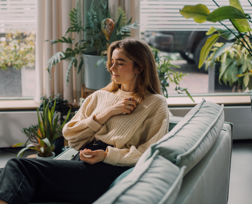 Een foto van een vrouw die op een bank zit met haar ogen dicht en de Pebbles technologie van Glimp in haar hand.