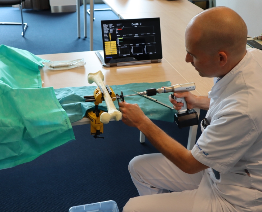Een foto van een dokter bij ZorgTech die met een boor door een nep bot gaat.